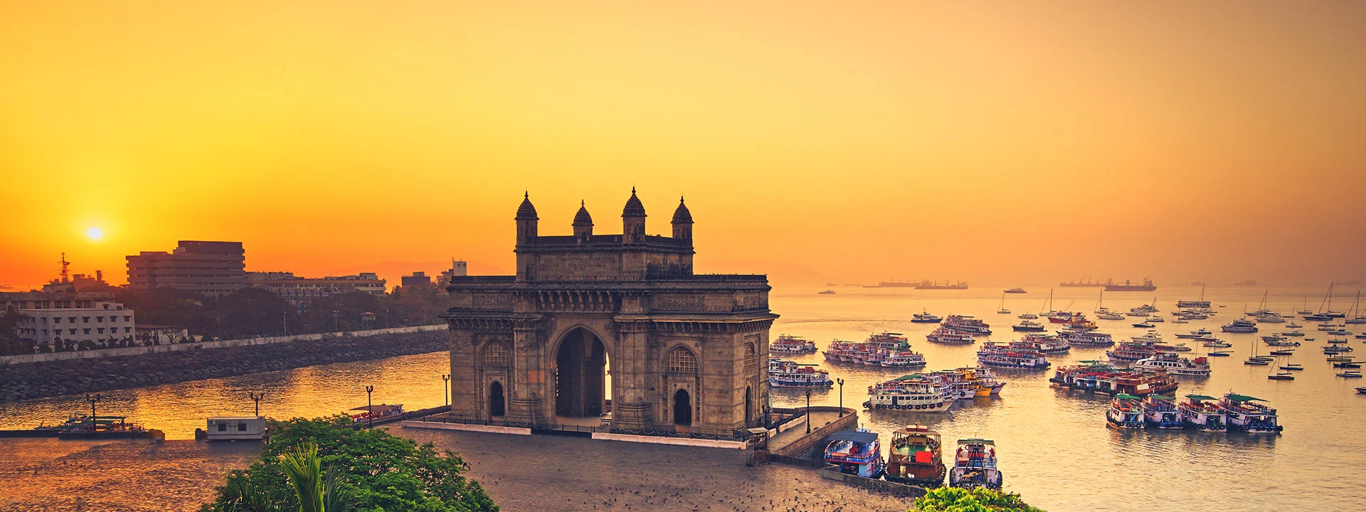 the gate of mumbai at sunset surrounded by colourful boats